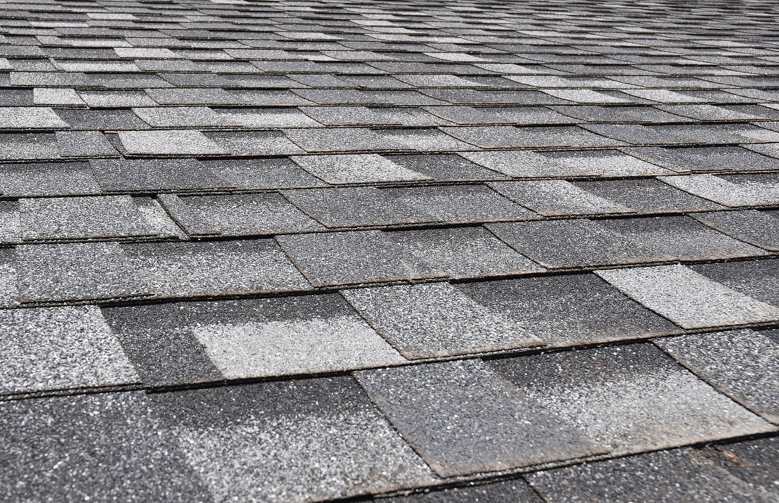 Close-up of gray asphalt shingles on a roof showing texture and layered pattern with varying shades