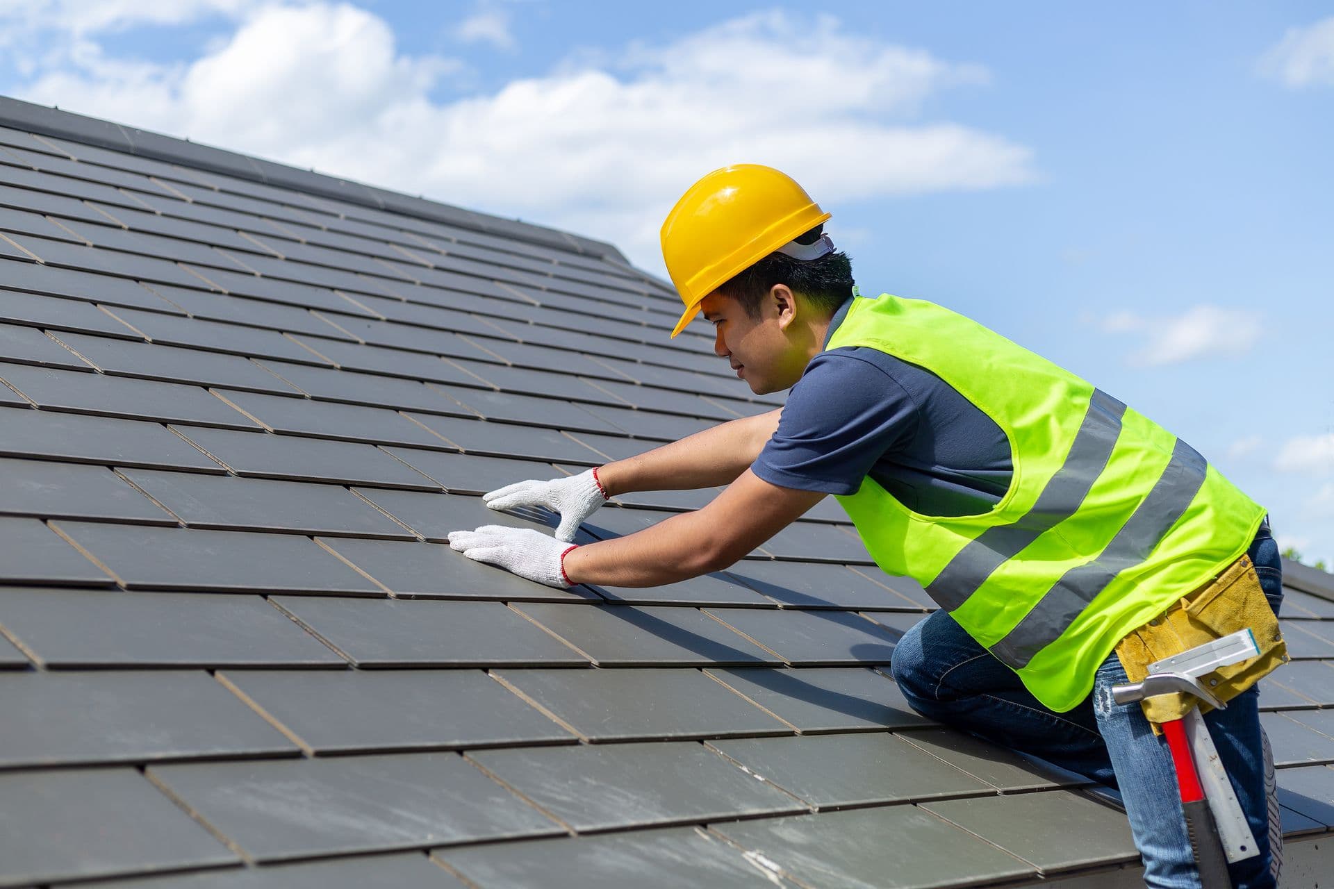 Roof repair, worker with white gloves replacing gray tiles or shingles on house with blue sky as background and copy space