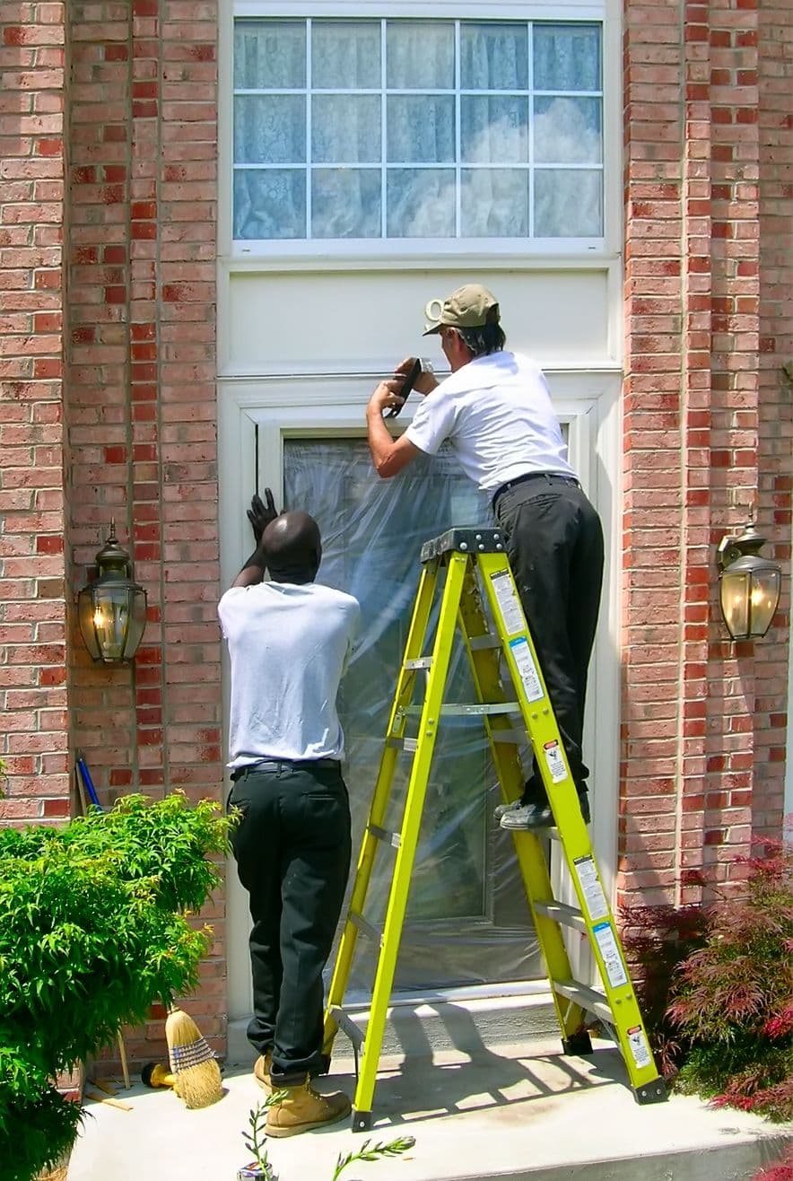 Two handymen installing an entry door on a brick house in the suburbs.