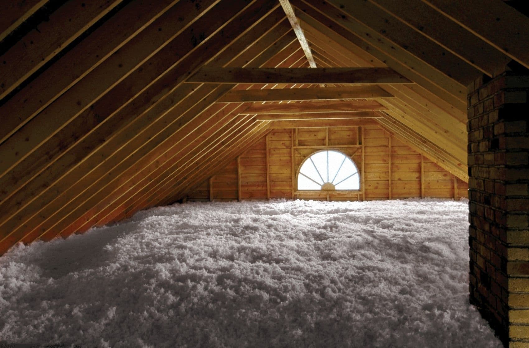 Attic space filled with white fiberglass insulation under wooden roof beams with a semicircular window at the far end