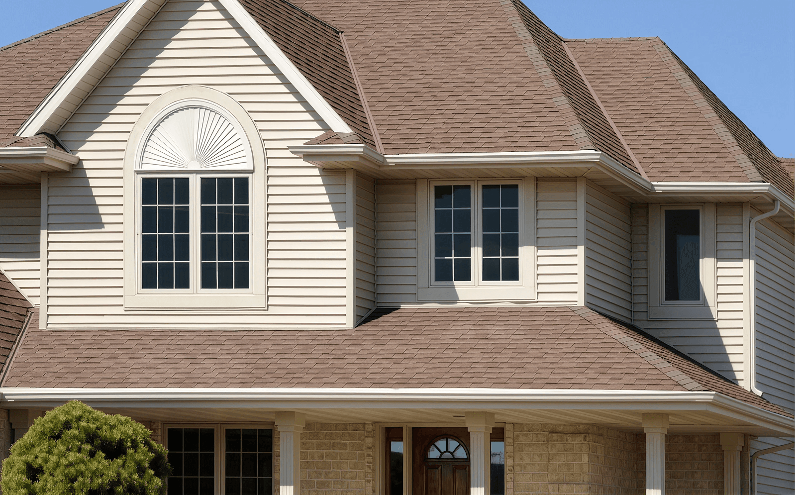 Exterior upper-story facade view of a suburban home featuring beige vinyl siding, a brown shingle roof, and white-framed multi-pane windows, including a large center window topped by an arched fan-shaped decorative element.