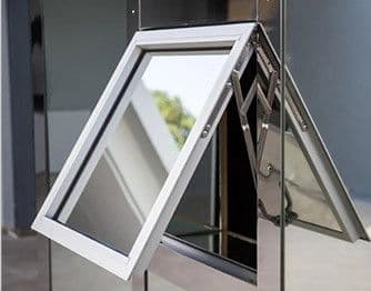 Close-up side view of a white-framed awning window hinged at the top and opening outward from the bottom via mechanical scissor arms, set into a reflective metallic building facade.